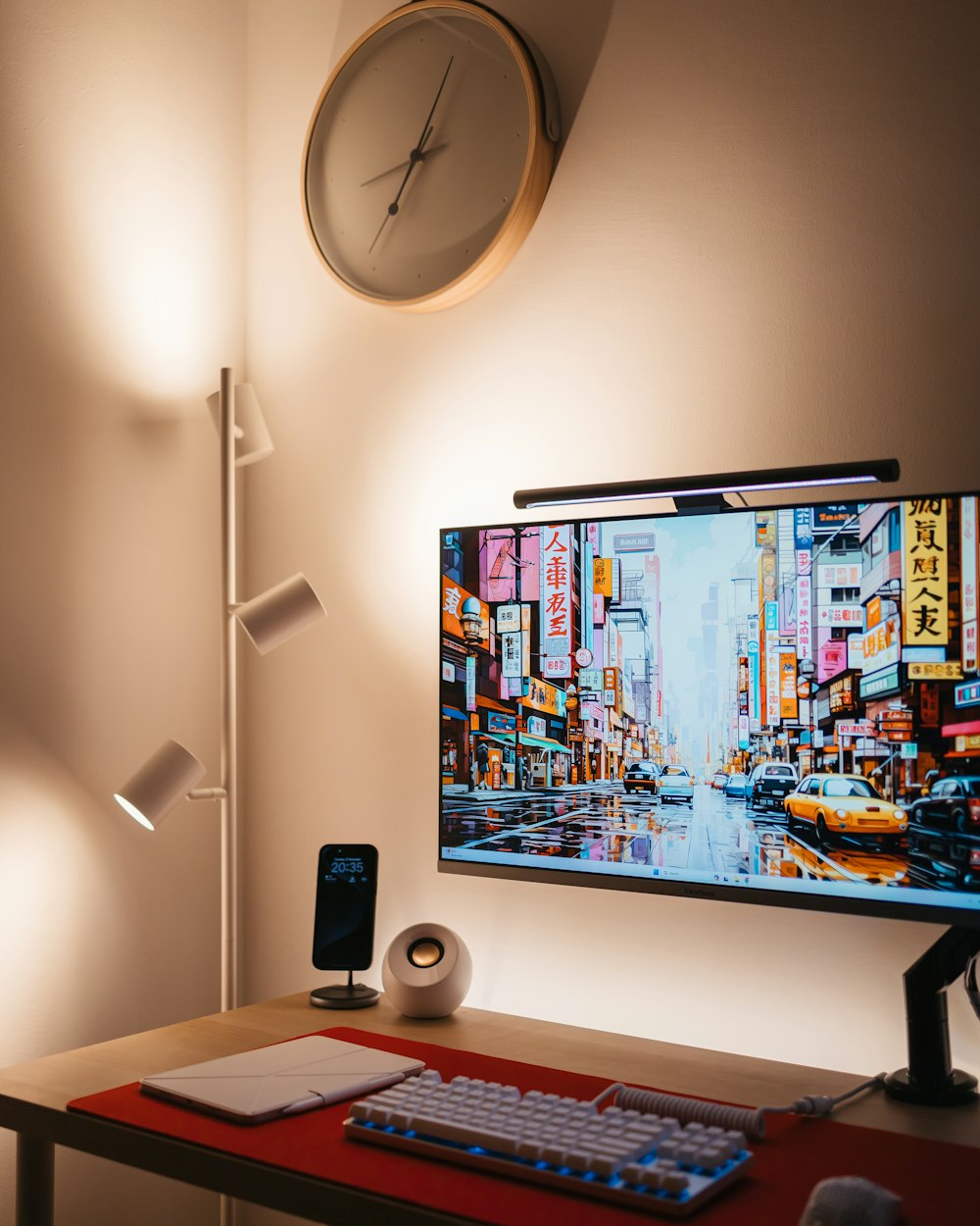 a desk with a keyboard, mouse, cell phone and a clock on the wall