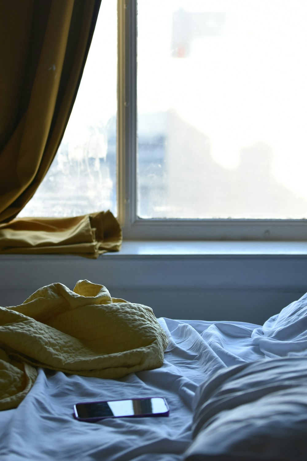 Un teléfono celular tirado en una cama junto a una ventana