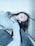 A person is reclining on a surface with closed eyes, appearing to be in a relaxed state. The individual is wearing a light-colored top and gray jeans. The setting appears minimalistic and dimly lit, creating a serene and calm atmosphere.