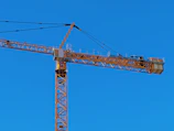 A tall crane lifting steel beams against a clear blue sky in Bali.