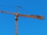 Yellow mobile crane lifting steel beams at a Dubai construction site under clear skies.