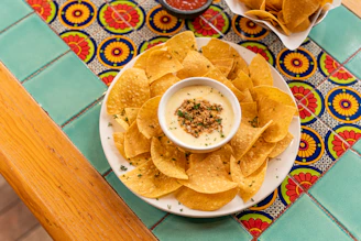 Close-up of a creamy dip with shredded dried meat served with crunchy totopos on a rustic wooden table.