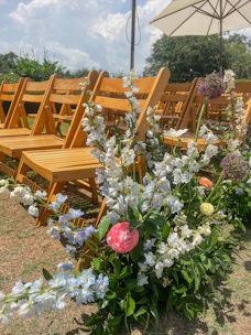 Guests seated on wooden chairs adorned with wildflowers under a canopy of clouds.
