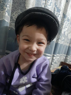 A smiling child wearing a winter outfit with a unique printed design in shades of purple.