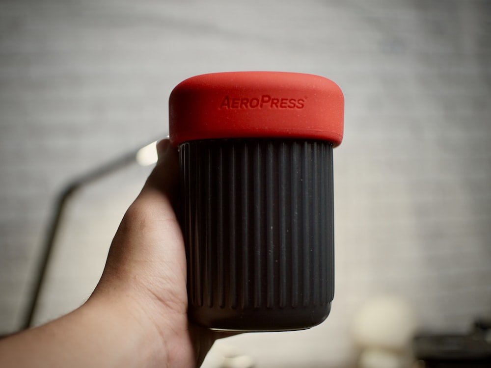 a hand holding a red and black coffee cup