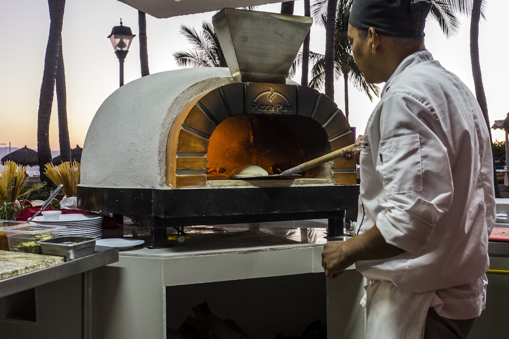 a man standing in front of a pizza oven