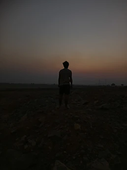 Silhouetted figure standing atop a rocky outcrop under a twilight sky with golden hues.