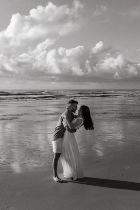 Couple sharing a romantic moment by the shore with gentle waves and soft natural light