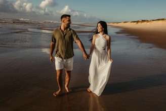 a man and woman walking on the beach holding hands