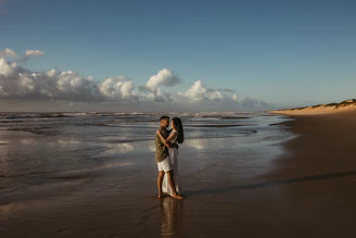 a man and woman standing on a beach next to the ocean