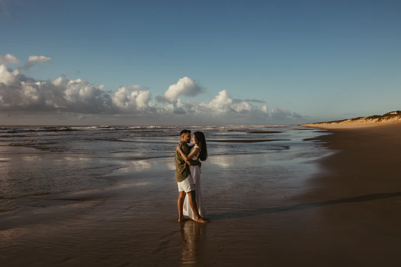 a man and woman standing on a beach next to the ocean