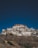 A monastery complex with traditional white buildings and colorful accents is perched on a rocky hillside under a clear blue sky.