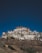 A monastery complex with traditional white buildings and colorful accents is perched on a rocky hillside under a clear blue sky.