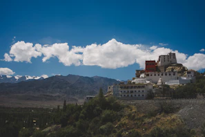 An elevated perspective showing a pristine Bhutanese monastery perched on the edge of a cliff beneath a vivid blue sky.