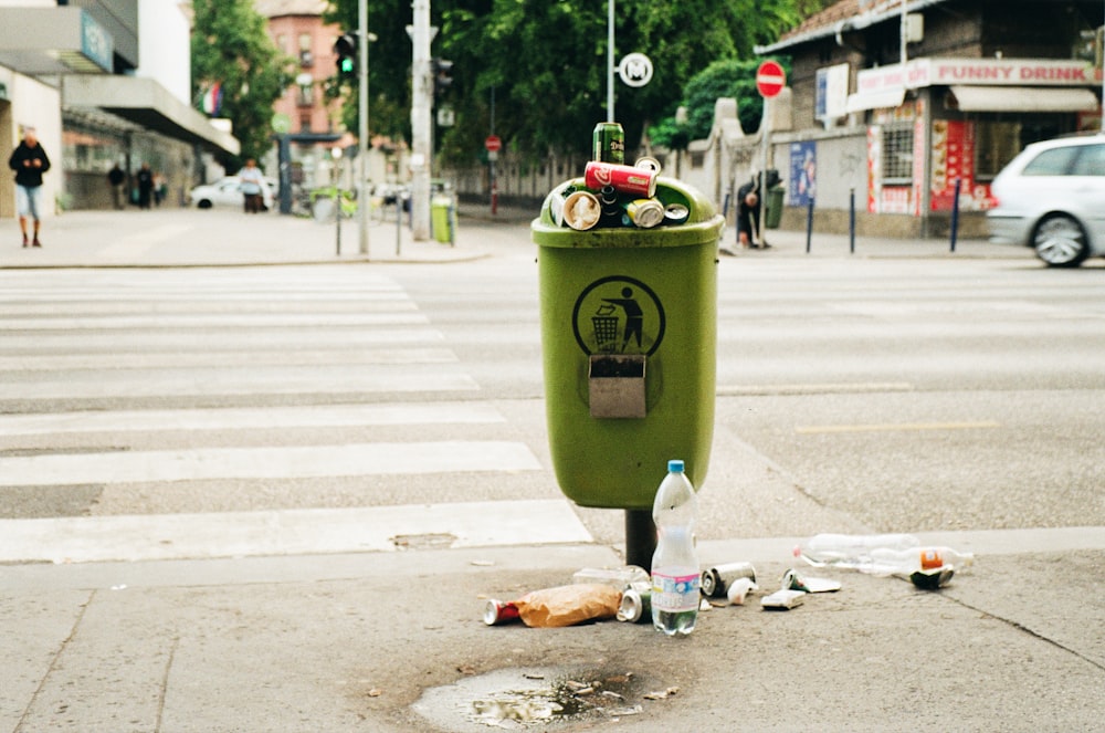 a green trash can sitting on the side of a road