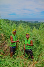 two men in green vests standing in tall grass