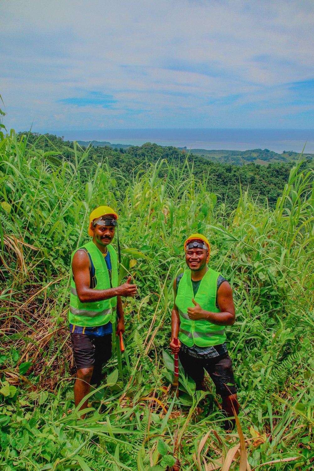 two men in green vests standing in tall grass