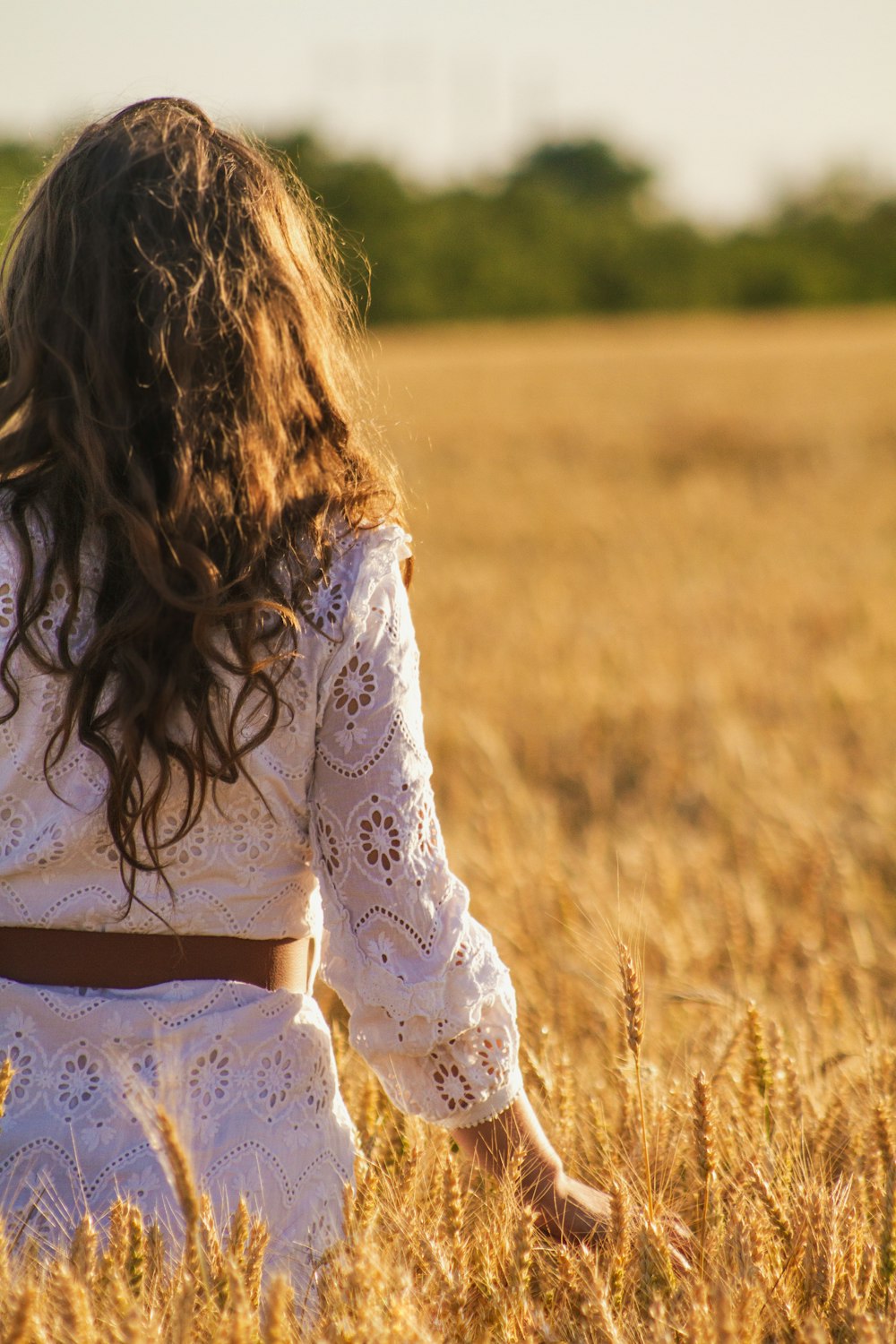a girl in a white dress walking through a wheat field