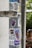 A metal pole covered with a variety of colorful stickers. These include cartoon characters, graffiti tags, and text with bold designs. The stickers appear to have been collected over time, showcasing playful and artistic themes. In the background, two people are vaguely visible, adding a touch of urban life to the scene.
