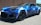 A sleek sports car with a custom paint job showcasing vibrant blue lightning patterns on its body, parked on a street with a brick building in the background. The car has a modern aerodynamic design with tinted windows and large black wheels.