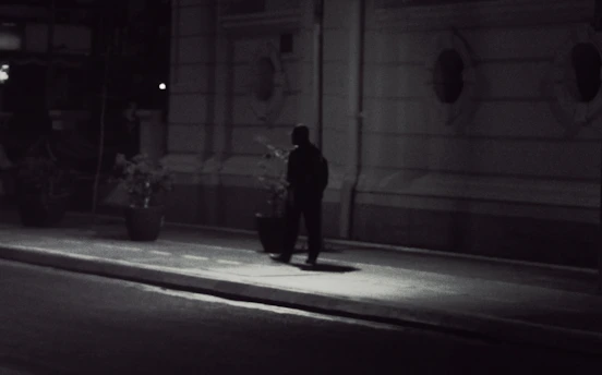 A shadowy figure walking cautiously down a dimly lit urban street at night.