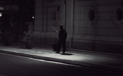 A cinematic scene showing a shadowed figure walking through a city at dusk.