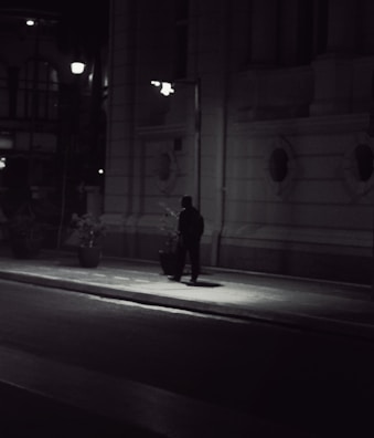 A shadowy figure sitting quietly, silhouetted against the faint glow of city lights above.