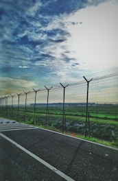 A sturdy galvanized wire fence surrounding a lush green farm under a clear blue sky.