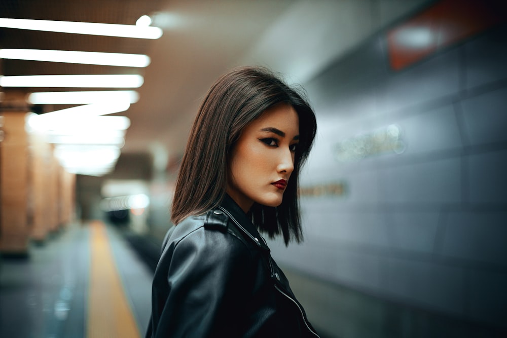 a woman in a black leather jacket standing in a subway station