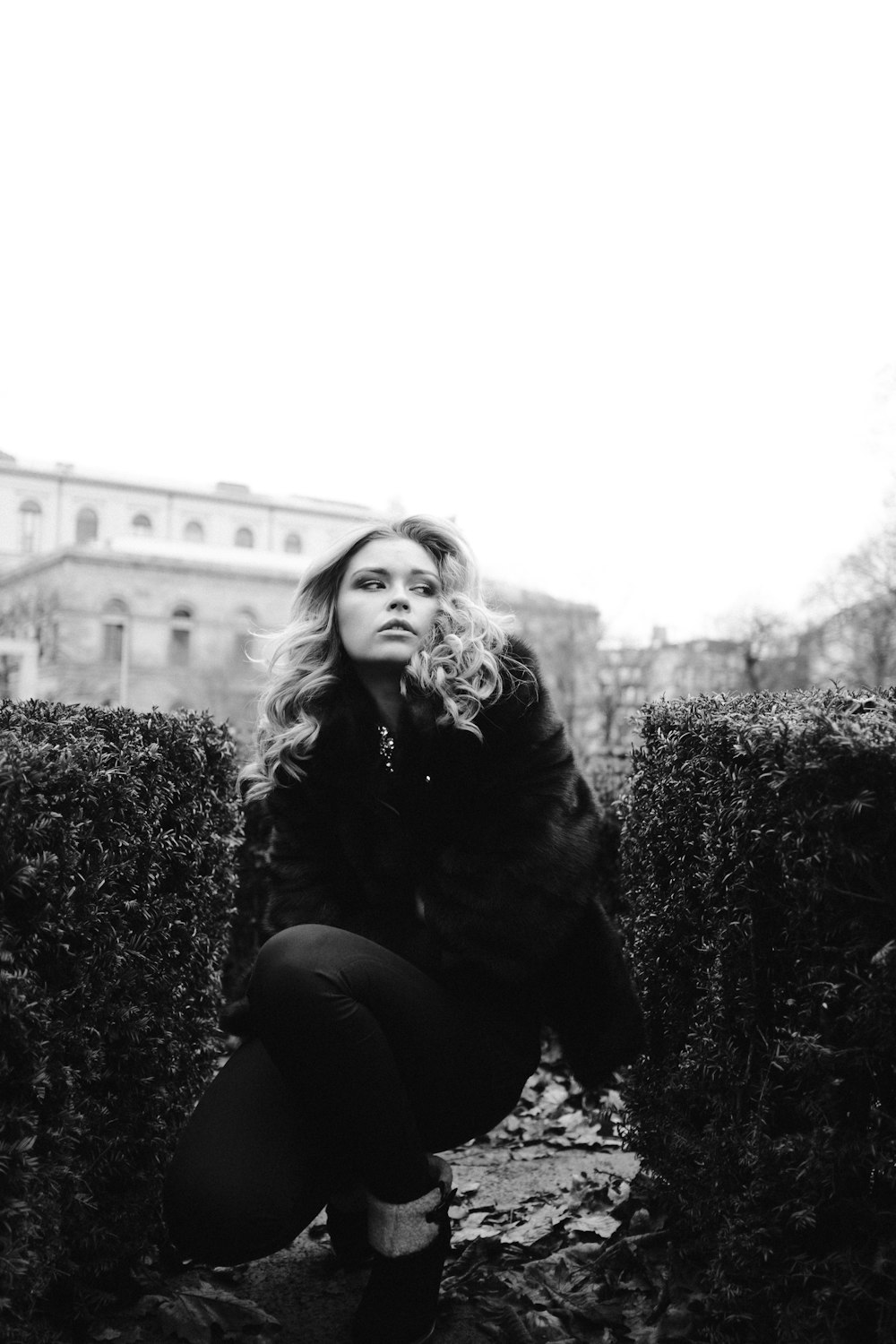 a woman kneeling down in front of a hedge