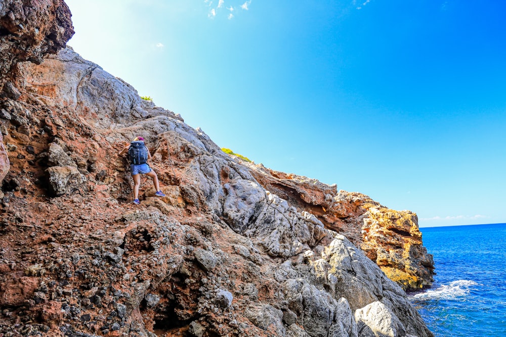 a man climbing up the side of a mountain next to the ocean