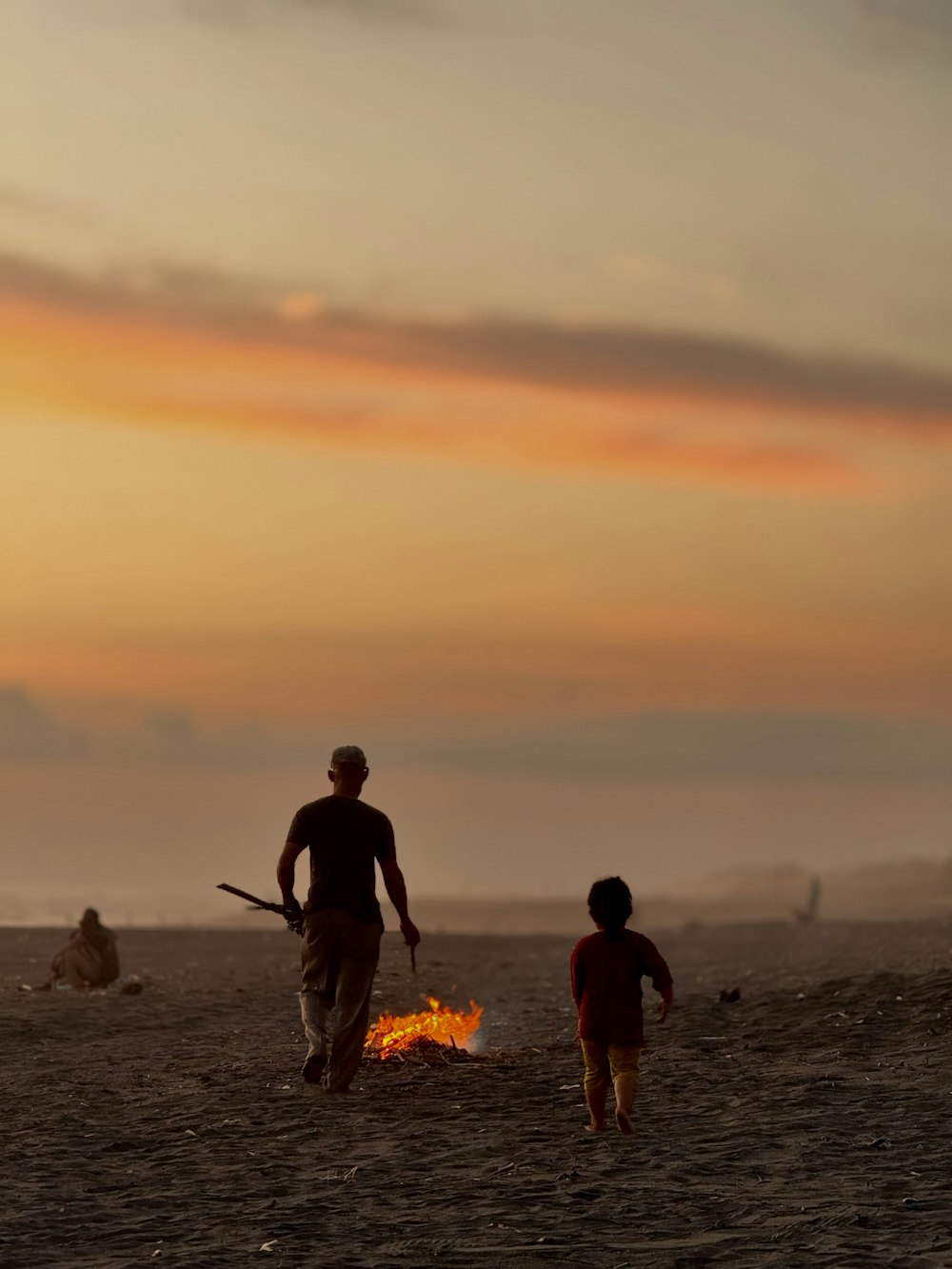 a man and a child standing on a beach next to a fire