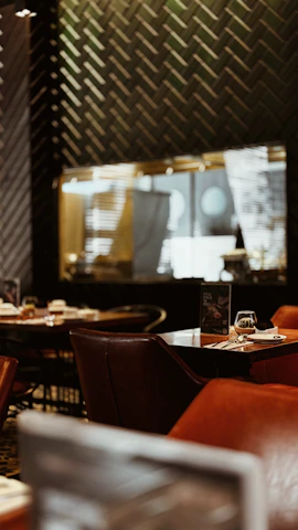 Cozy interior of noirflame with dark elegant tones and warm lighting highlighting a table set with smashed burgers and cocktails.