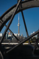 A sharp photo of the iconic CN Tower framed by a clear blue sky with a subtle maple leaf watermark.