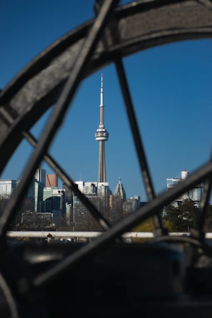 A sharp photo of the iconic CN Tower framed by a clear blue sky with a subtle maple leaf watermark.