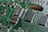 A close-up view of a green circuit board featuring various components including integrated circuits, resistors, and capacitors interconnected with intricate pathways. The surface is covered with small, rectangular black chips marked with white text, and metallic connections. The focus highlights the complex design typical of an electronic device's internal structure.
