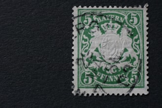 A vintage green postage stamp with a crowned emblem in the center and the word 'BAYERN' at the top. The denomination of 5 is printed in each corner of the stamp, with 'PFENNIG' at the bottom. The design includes intricate patterns and a cancelation mark indicating prior use.