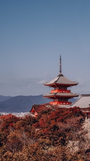 A serene view of a traditional Japanese pagoda framed by autumn leaves under a clear blue sky.