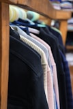 Several jackets are neatly hung on a wooden rack, showcasing a variety of colors and textures. The focus is on the shoulders and upper part of the jackets, with a blurred background that suggests a store setting.