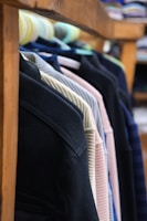 Several jackets are neatly hung on a wooden rack, showcasing a variety of colors and textures. The focus is on the shoulders and upper part of the jackets, with a blurred background that suggests a store setting.