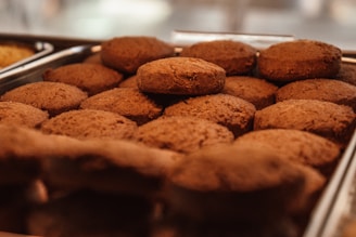 A tray filled with freshly baked brown cookies arranged in a neat pattern. The lighting highlights the texture and warmth of the cookies, suggesting they may still be warm from the oven.