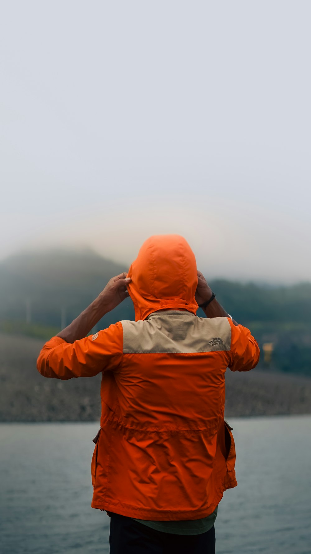 a person in an orange jacket looking out over a body of water