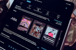 A close-up view of an iPad screen displaying an application interface in dark mode, featuring text in Russian and several graphics related to the app. The screen includes sections for ratings, language, size, and version history. There are preview images showcasing artistic designs and animations.
