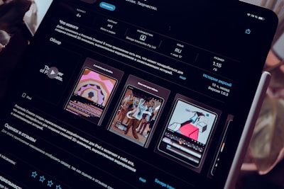 A close-up view of an iPad screen displaying an application interface in dark mode, featuring text in Russian and several graphics related to the app. The screen includes sections for ratings, language, size, and version history. There are preview images showcasing artistic designs and animations.