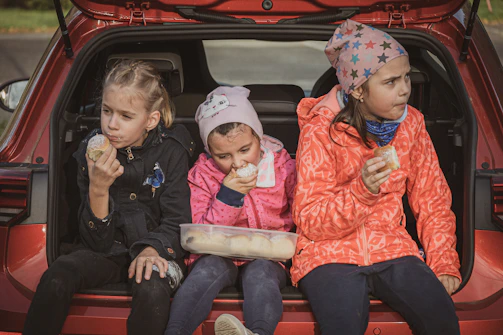 Children enjoying popcorn and laughter on a cozy blanket in front of a car.