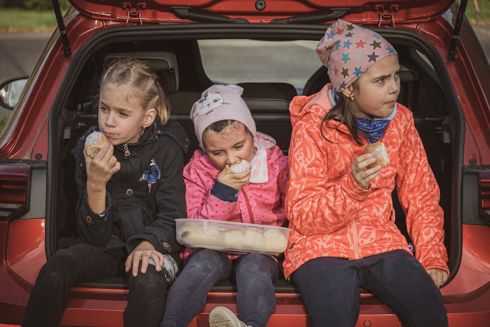 three little girls sitting in the back of a red car