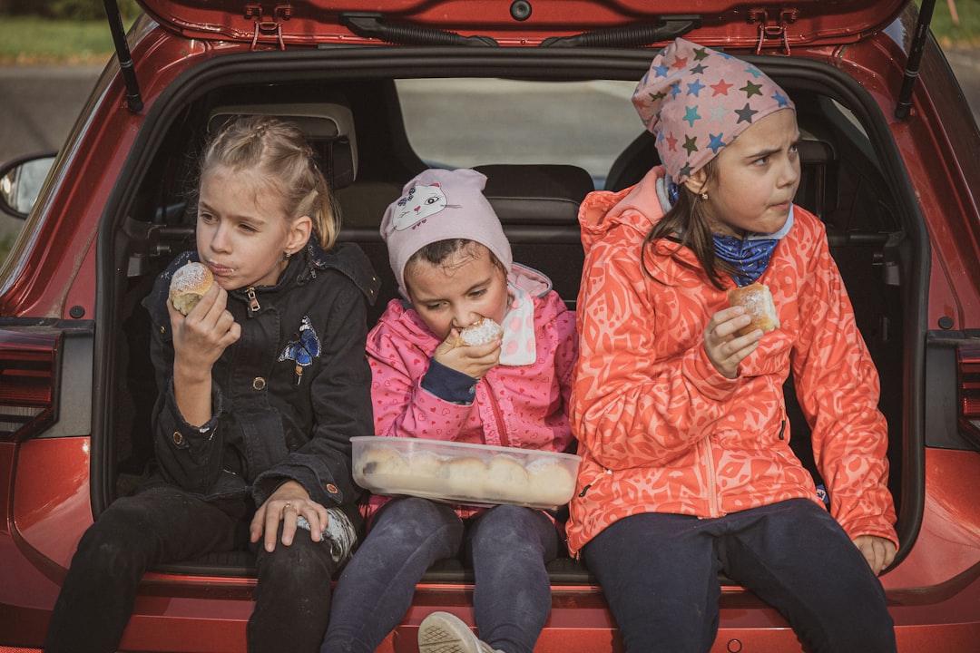 three little girls sitting in the back of a red car, three girls eating buns in the trunk of a car