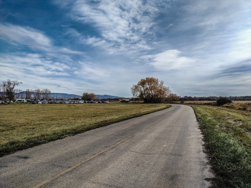 an empty road in a grassy field under a blue sky