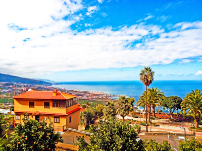 A charming coastal house with a bright blue sky and palm trees nearby.