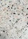 A terrazzo surface features an uneven distribution of multicolored stone chips embedded in a cementitious base. The chips are predominantly black, pink, and white, contrasting against a light grayish-green background.